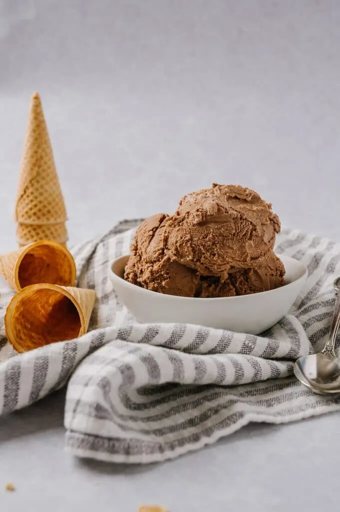 scoops of chocolate ice cream in a bowl with waffle cones in the background