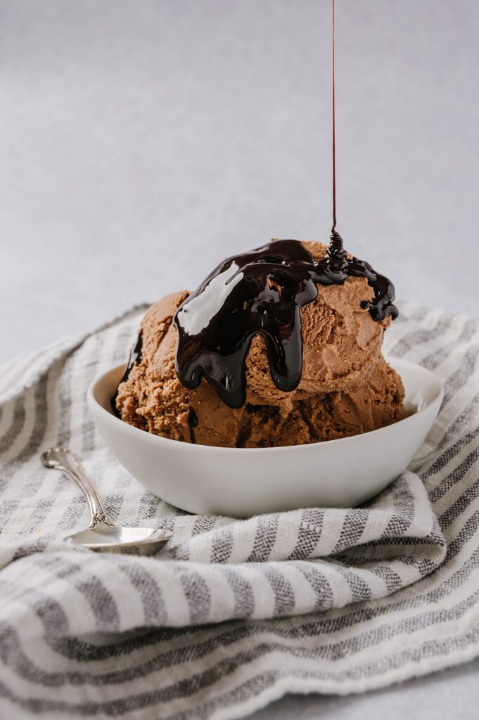 scoops of chocolate ice cream in a bowl with chocolate syrup being poured over the top