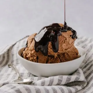 scoops of chocolate ice cream in a bowl with chocolate syrup being poured over the top