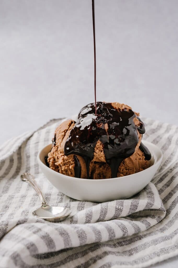 chocolate ice cream in a bowl with chocolate syrup being drizzled