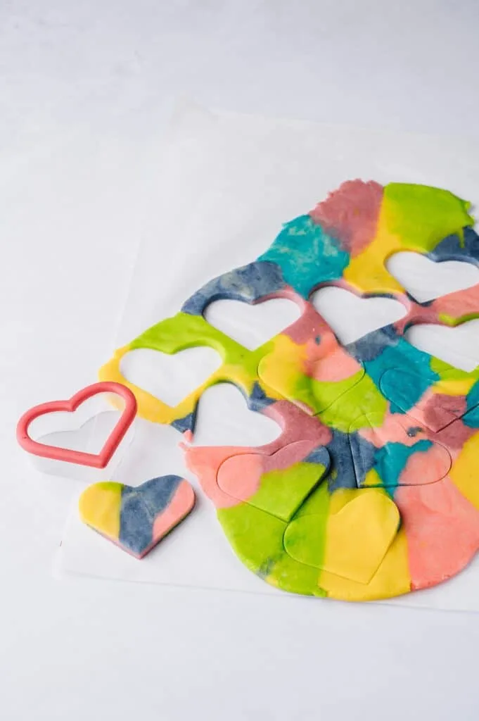 colored sugar cookie dough being cut out with a heart shaped cutter