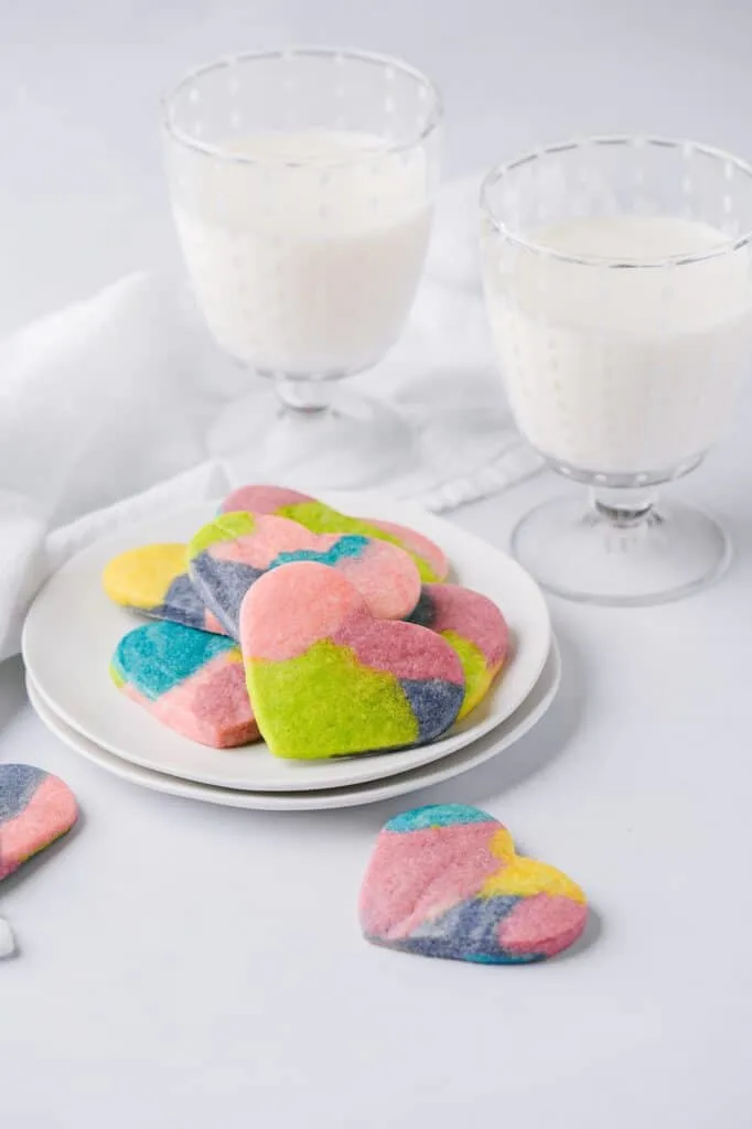multi colored heart shaped sugar cookies on a plate with two glasses of milk 