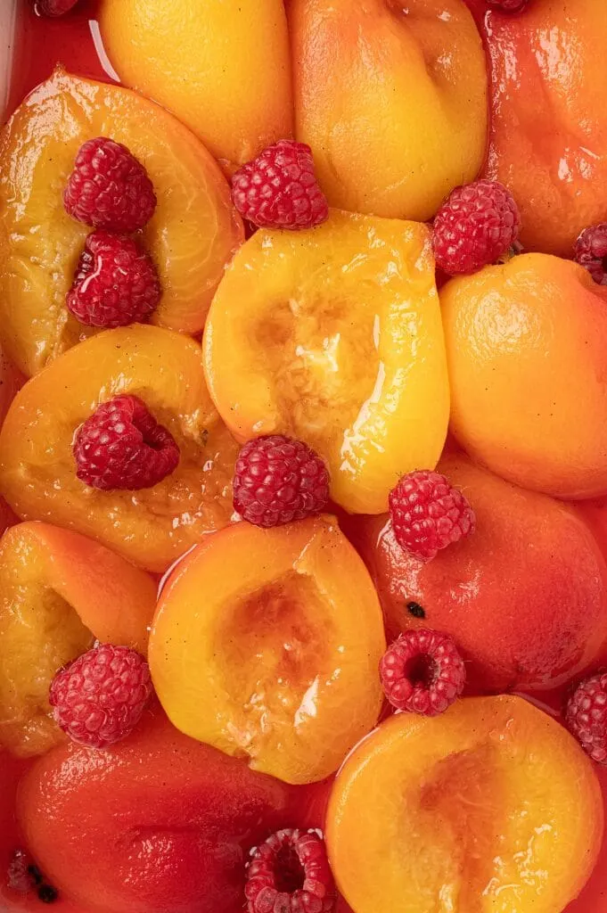 poached peaches with raspberries in a casserole dish