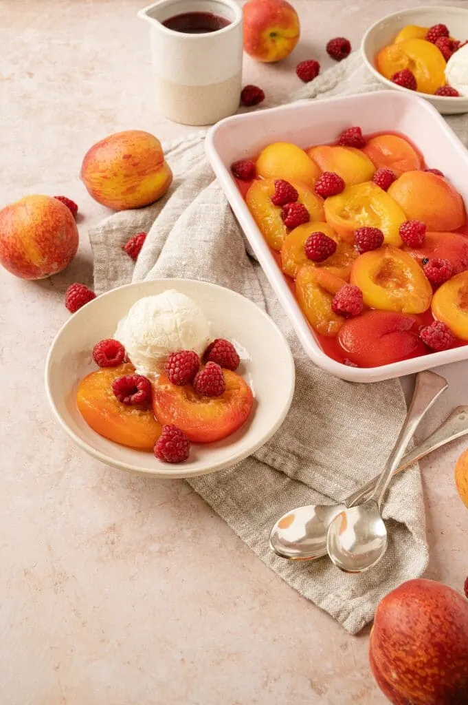 poached peaches with raspberries in a bowl with peaches and casserole dish behind