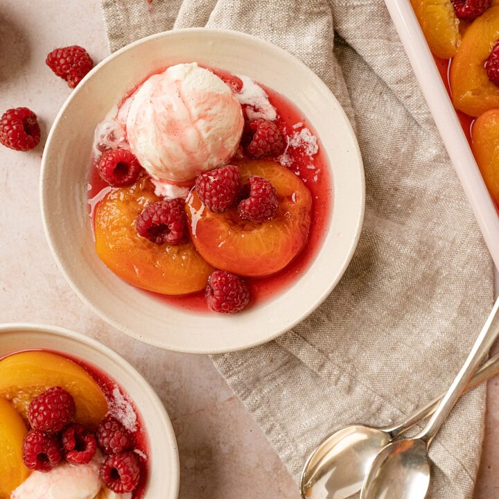bowl of poached peaches with raspberries with full dish in the background
