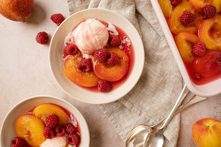 bowl of poached peaches with raspberries with full dish in the background