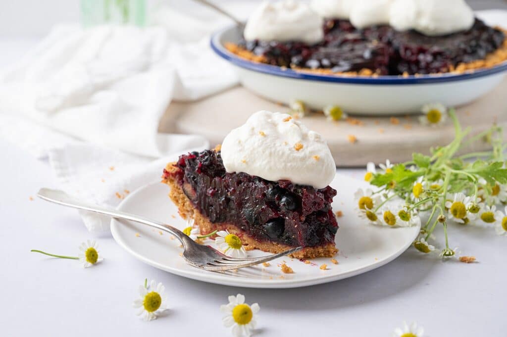 slice of blueberry pie on a plate with whipped cream and the whole pie in the background