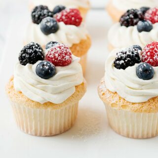 whipped cream on angel food cupcakes with berries and powdered sugar