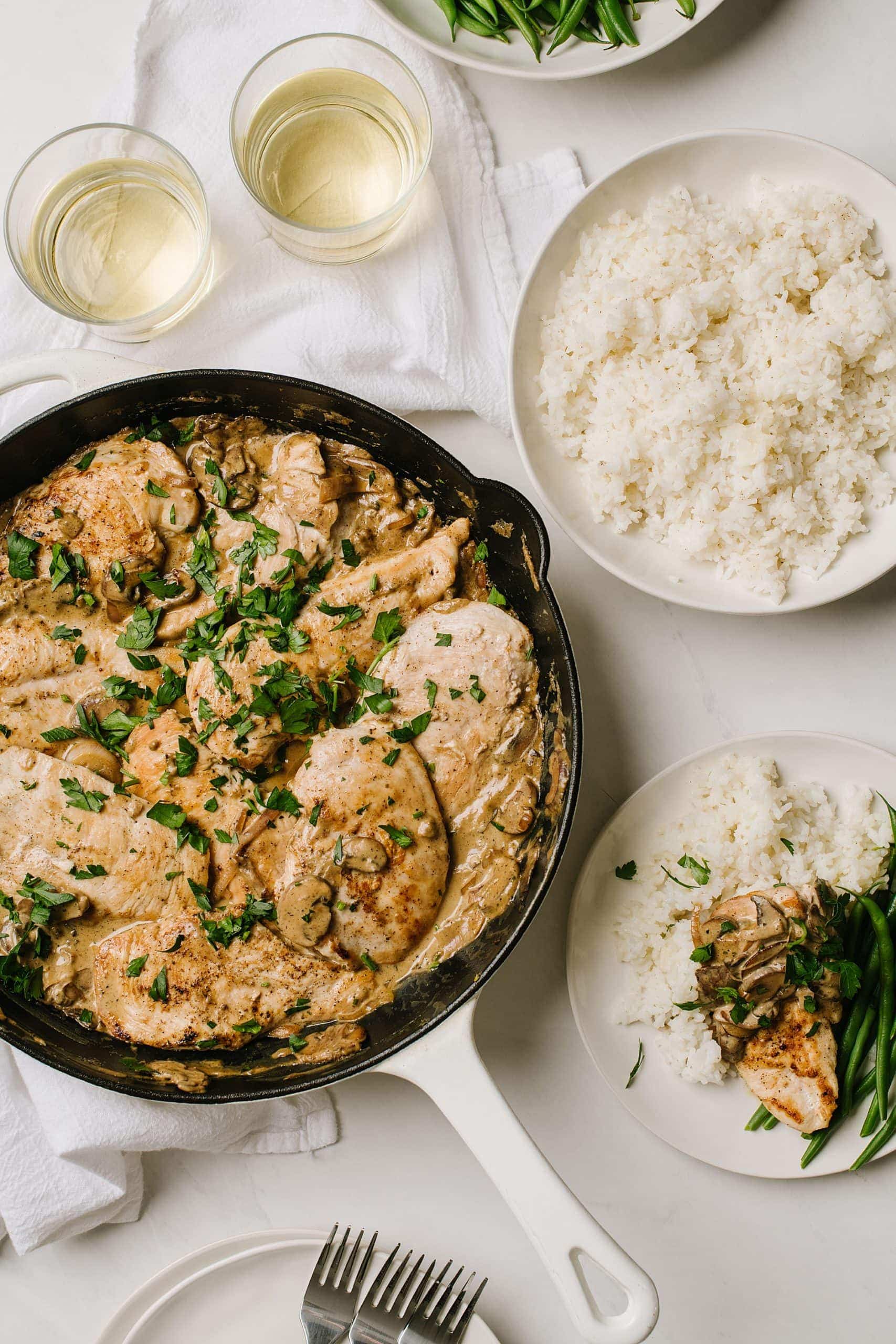 skillet of boursin chicken with glasses of wine and bowl of rice with a plate of chicken with green beans and rice