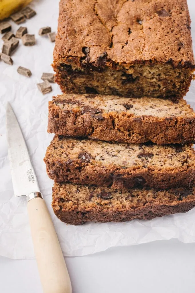 close up of best banana bread ever on parchment paper with chocolate chunks and a knife