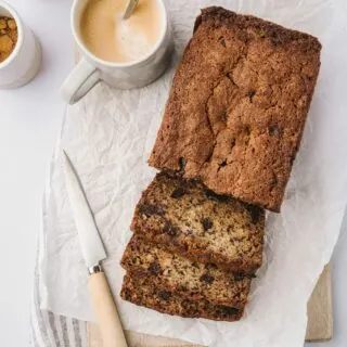 best banana bread ever on parchment paper with a knife and cups of coffee