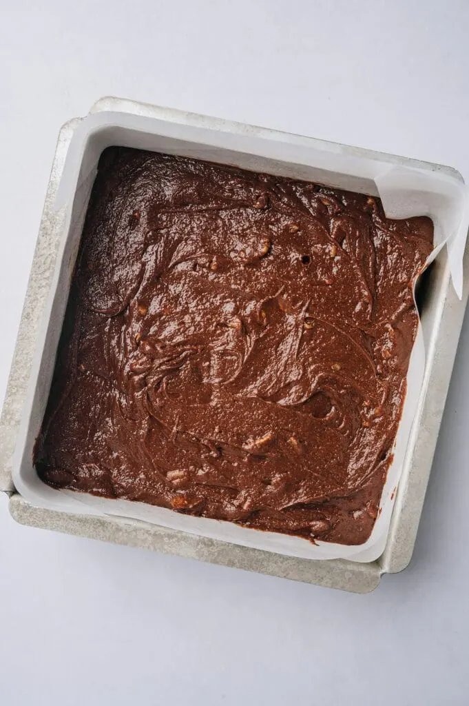 matt's crazy brownies batter in a pan lined with parchment paper ready to be baked