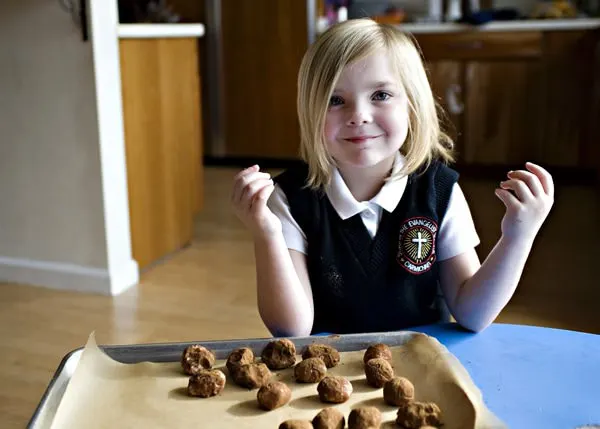 little girl with blonde hair making Irish potatoes candy