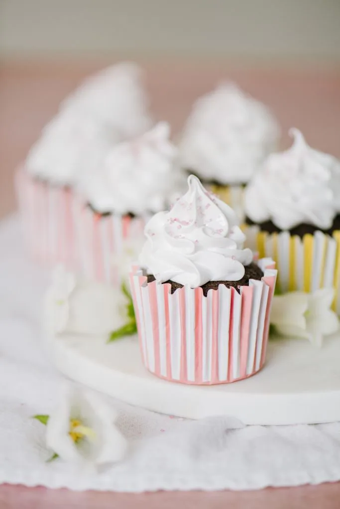 italian meringue boiled icing chocolate cupcakes on a platter with white flowers and pink sugar decorations
