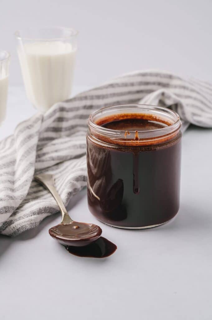 best chocolate sauce in a jar with a spoonful beside it and a glass of milk in the background