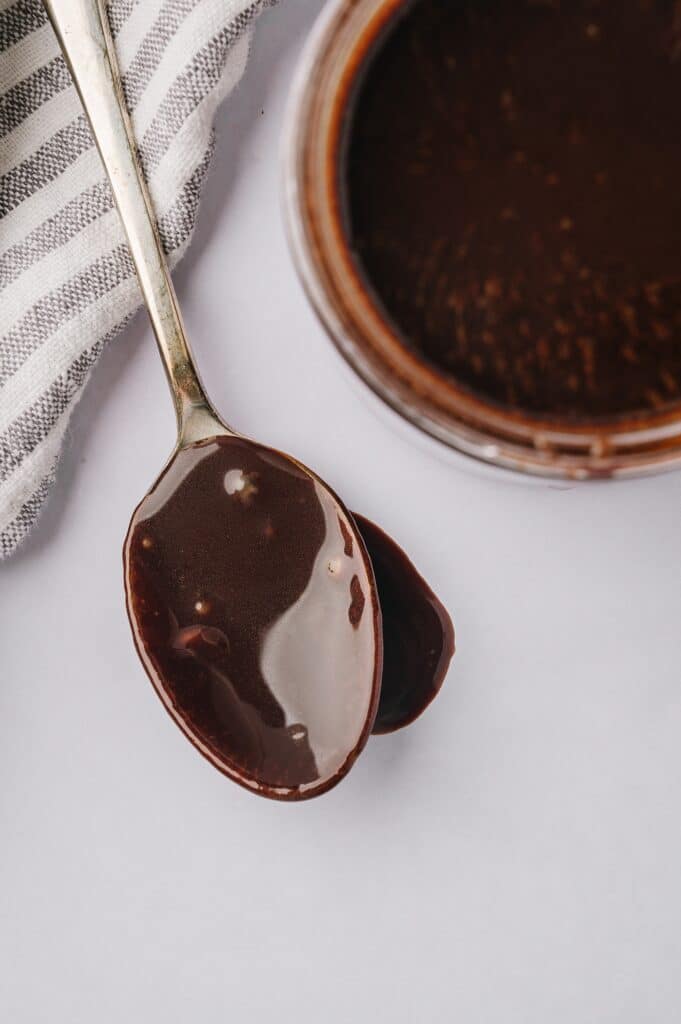 best chocolate sauce dripping from a spoon with a jar of sauce behind it