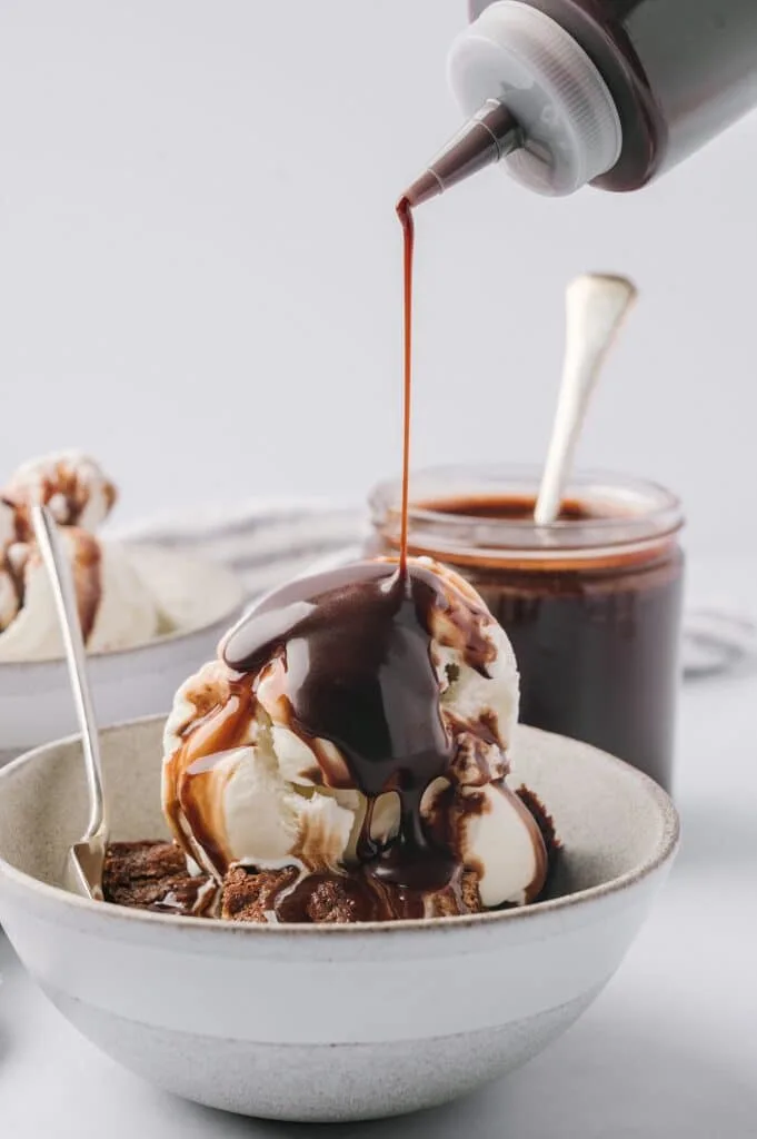 bowl of ice cream on a brownie with best chocolate sauce being drizzled on it