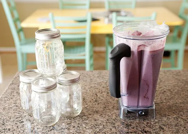 blender with homemade protein smoothie next to empty mason jars