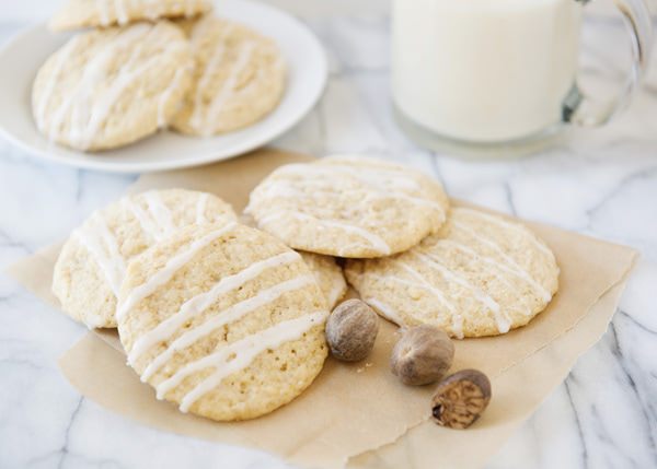 cookies drizzled with an eggnog glaze with nutmeg and a glass of milk on a white marble tabletop