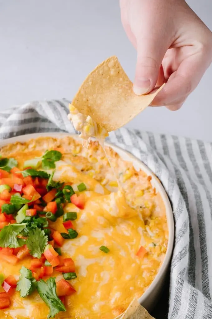 bowl of hot corn dip with a tortilla chip being dipped in