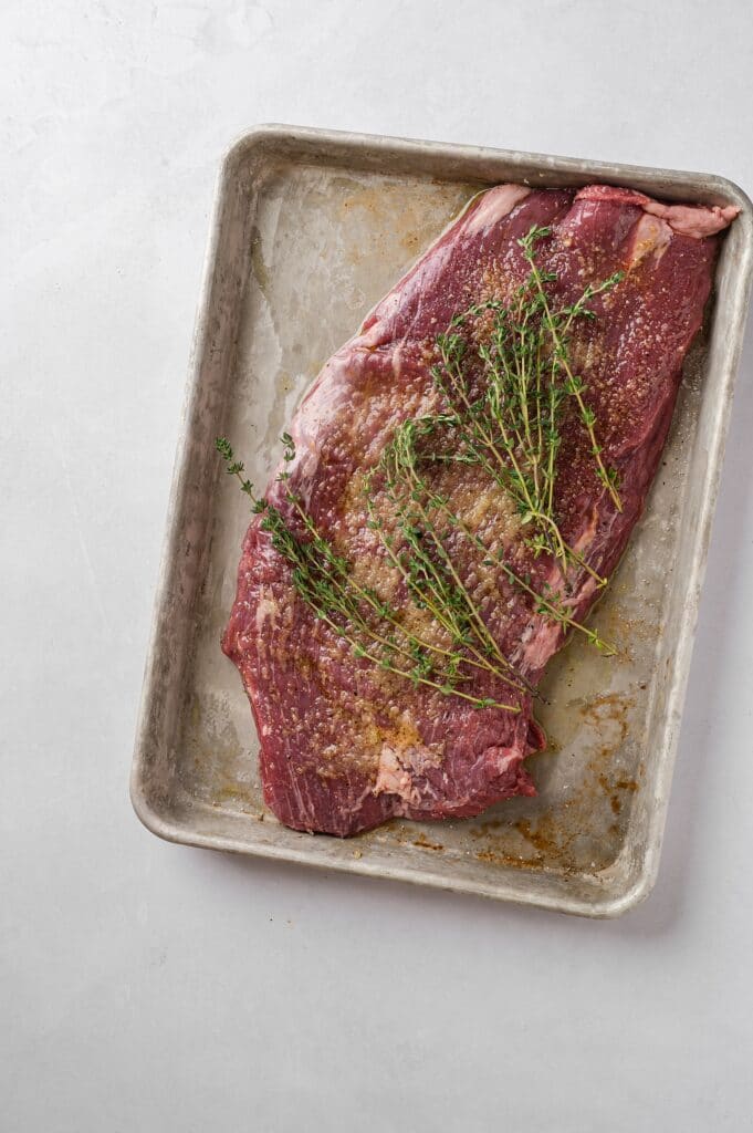 raw flank steak on a pan with  fresh herbs