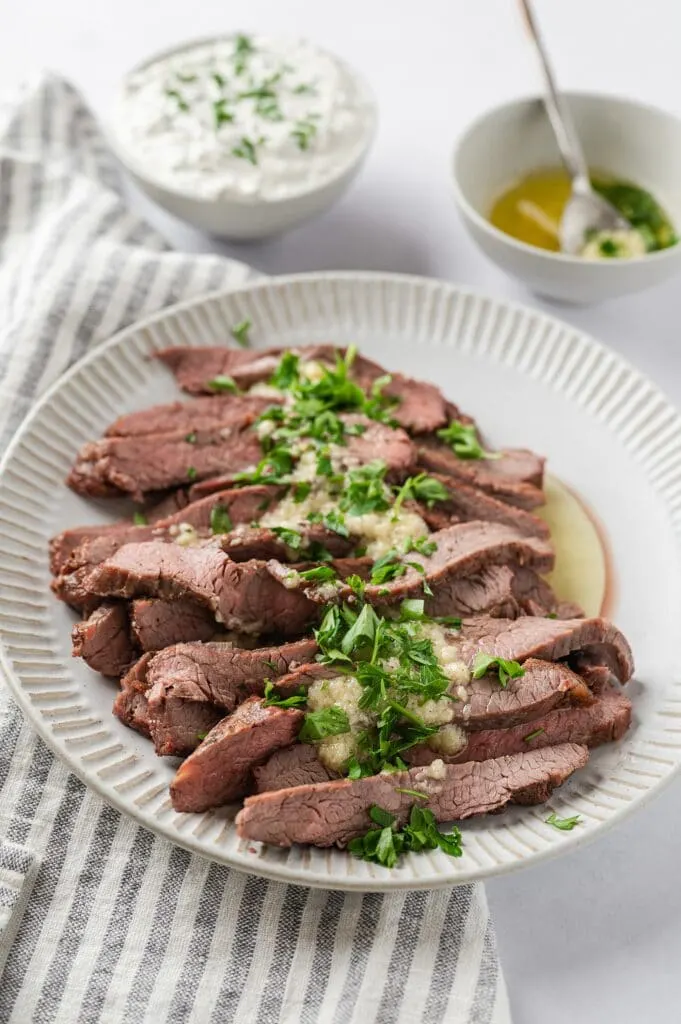 plate of flank steak with garlic butter sauce and sour cream and chives in the background