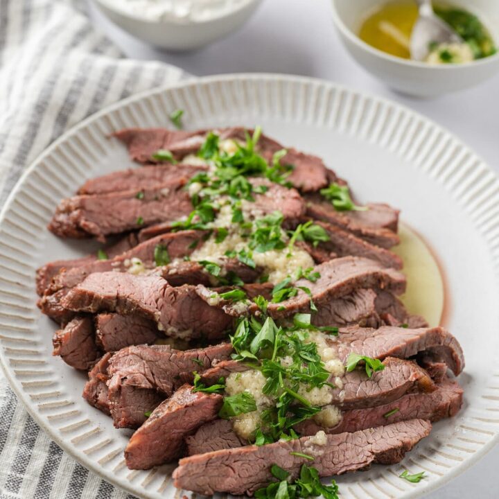 plate of flank steak with garlic butter sauce and sour cream and chives in the background