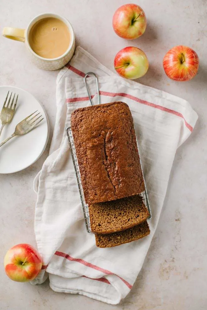 Applesauce Spice Bread on a rack with apples and coffee around it