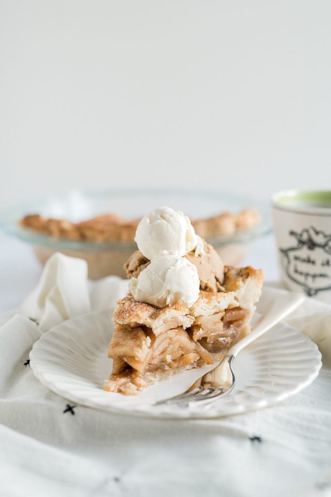 slice of Anna Olson Apple Pie on a plate with whip cream and full pie in the background