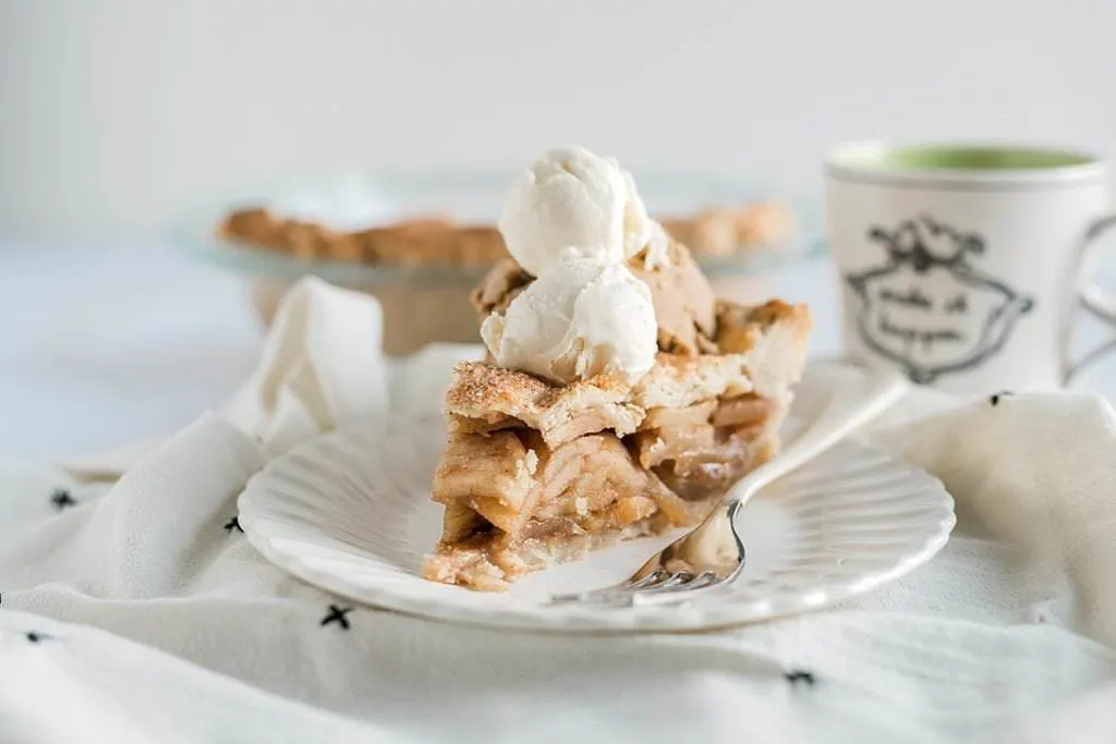 slice of Anna Olson Apple Pie with ice cream scoops and full pie in the background