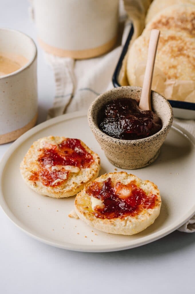 huckleberry english muffins on a plate with jam and dish of muffins and coffee in the background