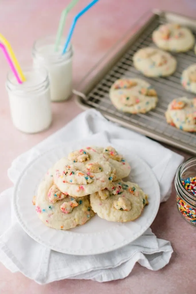 funfetti crumble cookies on a plate with glasses of milk and cooling cookies in the background