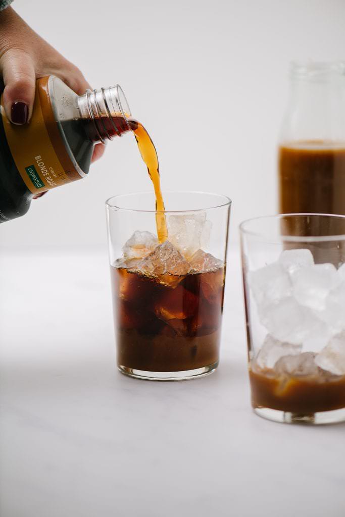 pouring cold brew into a glass of ice