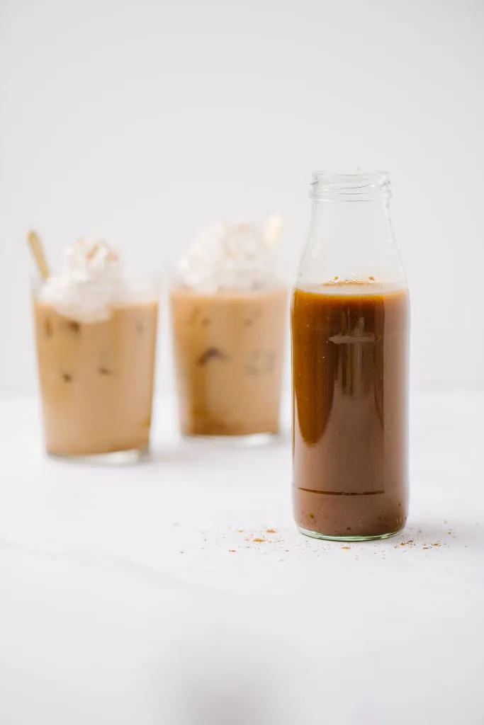 Dairy-Free Pumpkin Spice Syrup in a jar with two iced coffees in background.