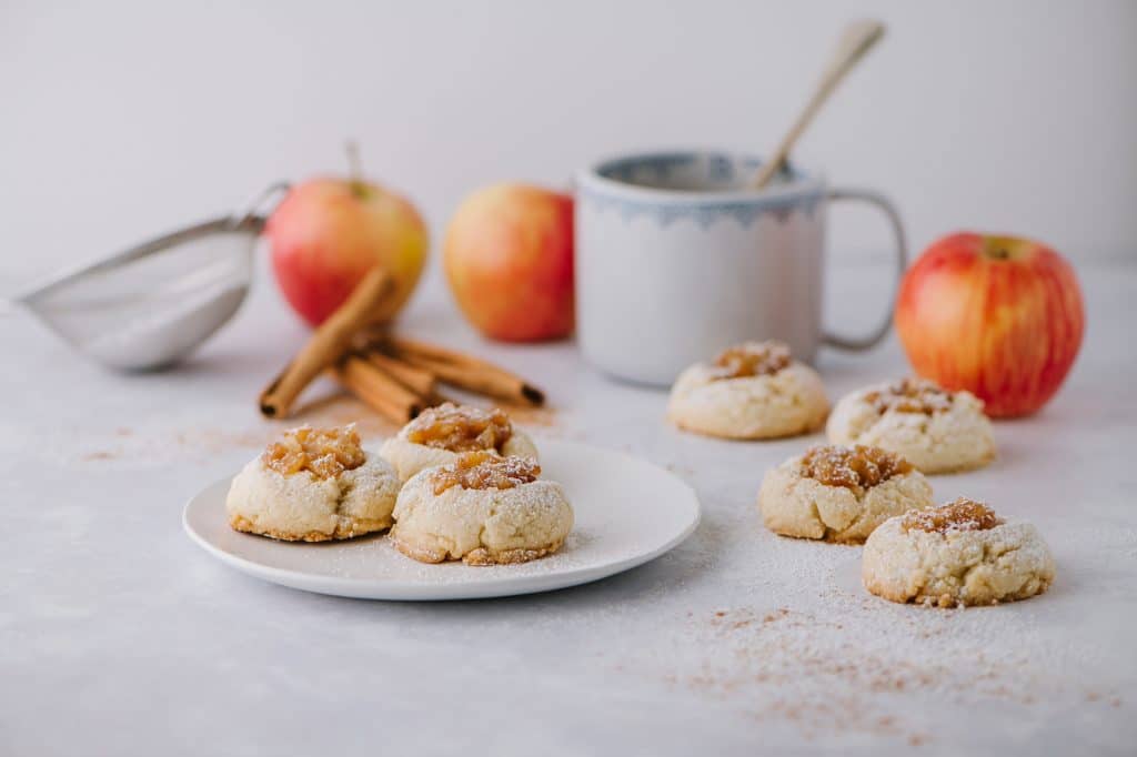 apple pie thumbprint cookies on a plate with apples and a mug in the background