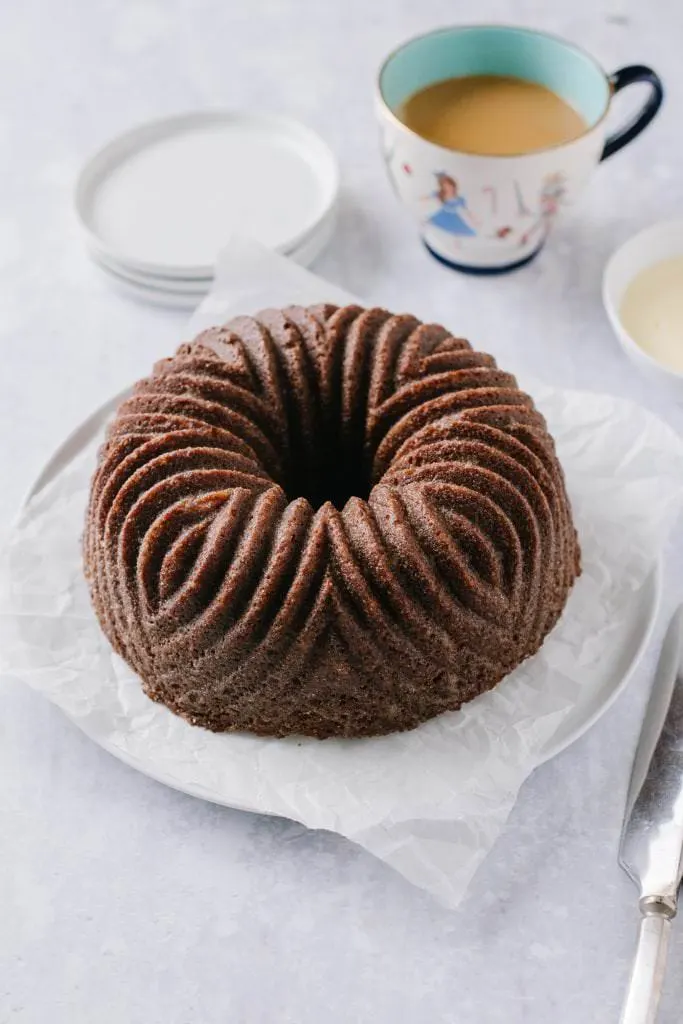 orange gingerbread bundt cake on a plate with a cup of coffee and a bowl of custard