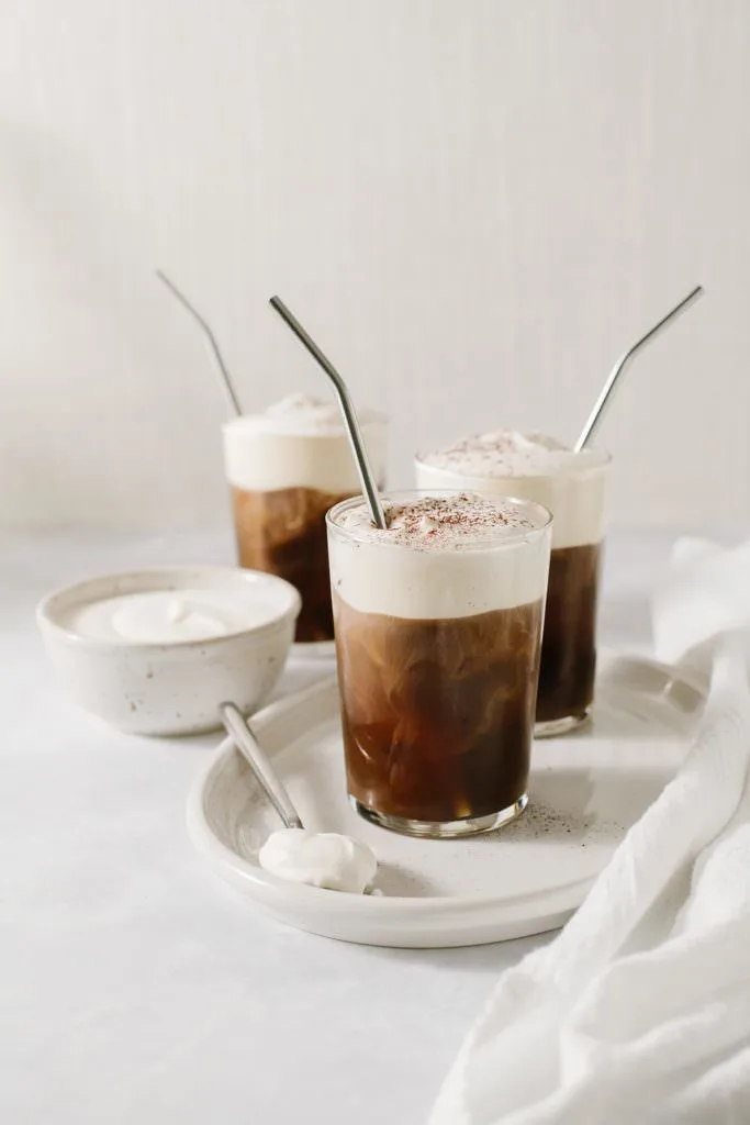 irish cream cold brew with metal straws on a tray with a bowl of cream
