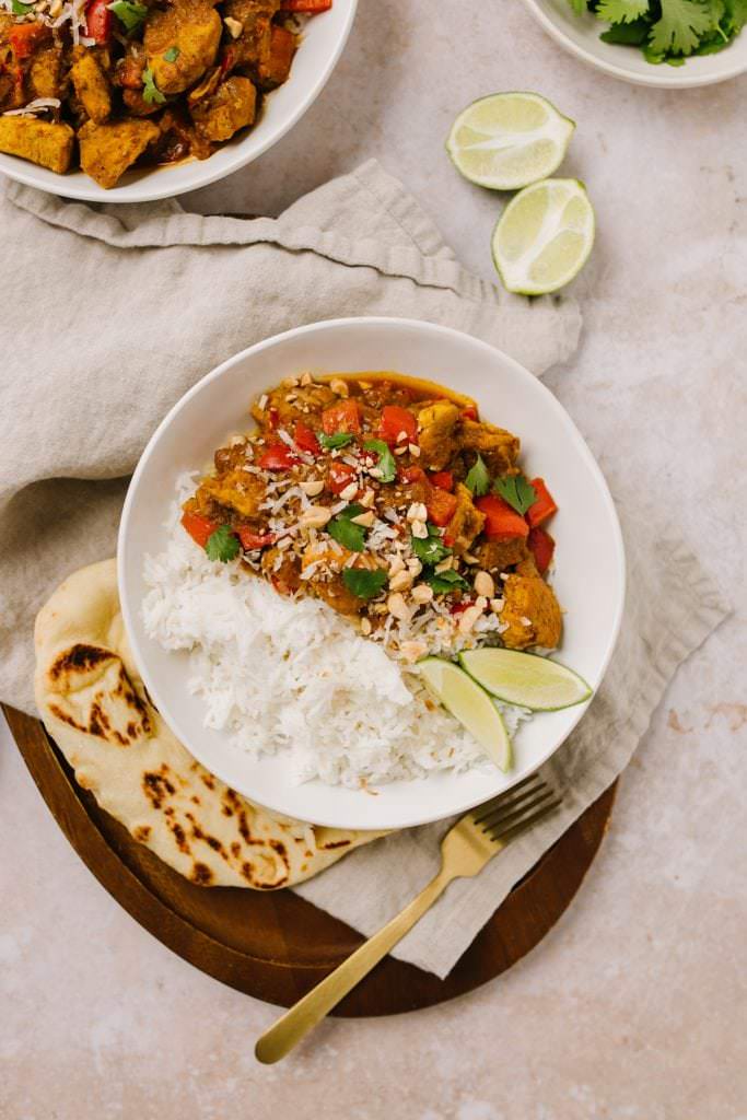 Easy Weeknight Chicken Curry Recipe in a bowl with rice with lime wedges and peanuts