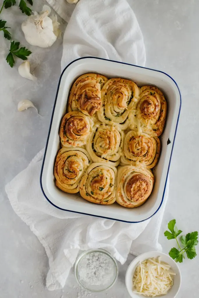 homemade rolls recipe in white ceramic baking dish with white towel and fresh garlic and parsley