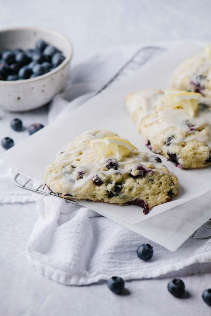 scones with blueberries and lemon glaze on parchment paper with blueberries in white bowl