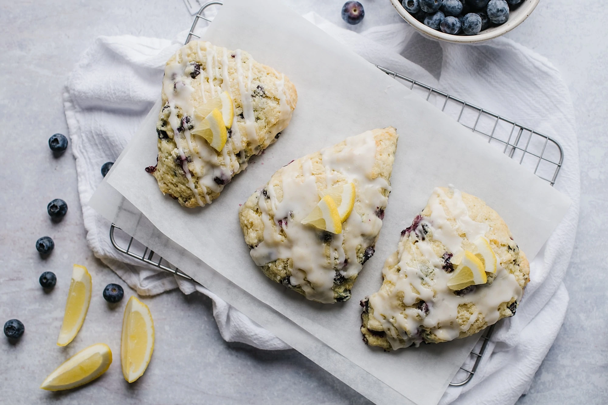 scones with blueberries and lemon glaze on parchment paper with blueberries in white bowl
