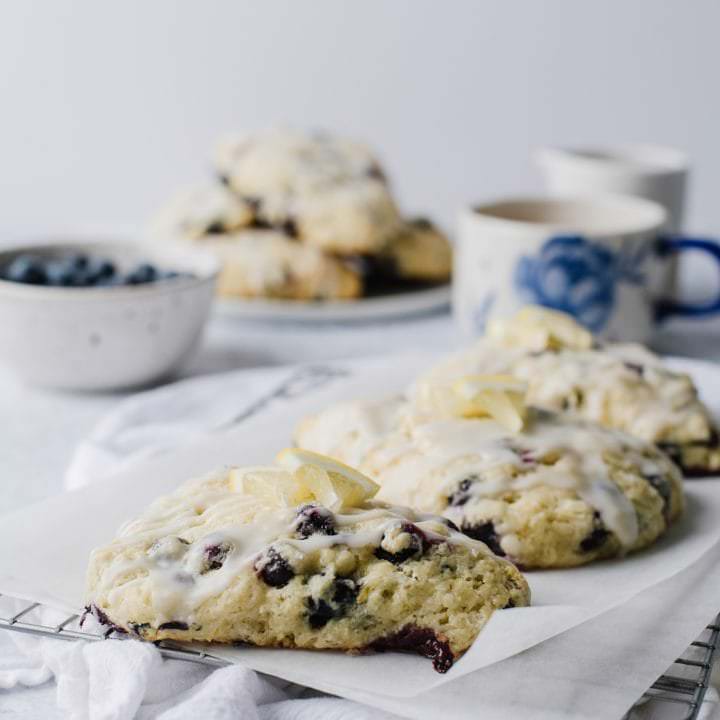 blueberry lemon scones on white plate with fresh blueberries in white bowl and mug of tea