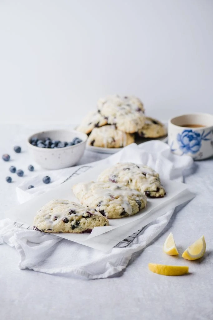blueberry lemon scones on white plate with fresh blueberries in white bowl and mug of tea