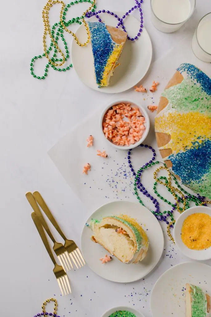 glazed, decorated and sliced Mardi Gras cake on white plate with gold forks and bead necklaces