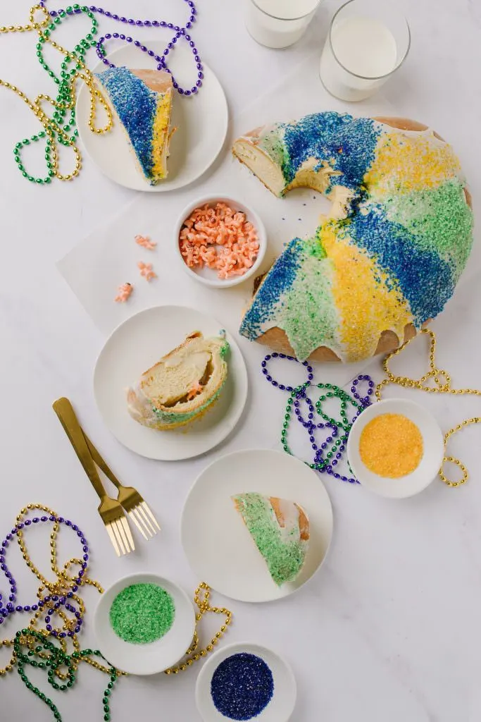 sliced king cake with slices on white plates, sanding sugar in bowls and pastry brush