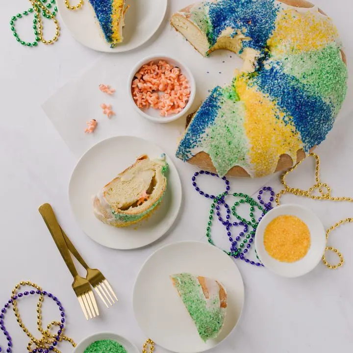 sliced king cake with slices on white plates, sanding sugar in bowls and pastry brush