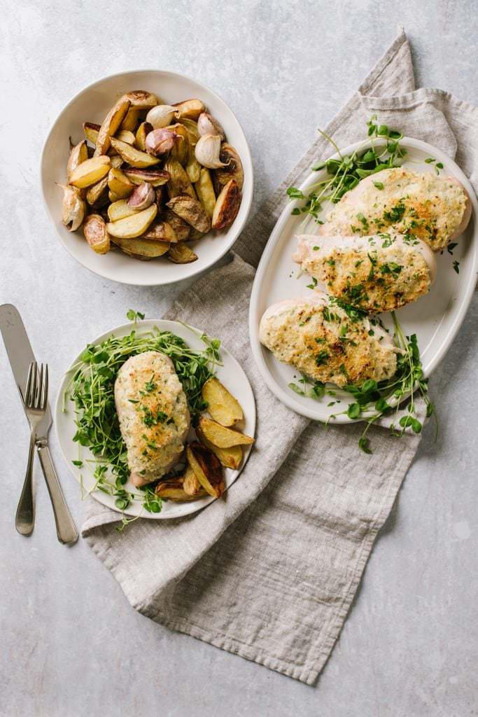 easy chicken dinner in white plate with greens, on white platter with bowl of potatoes