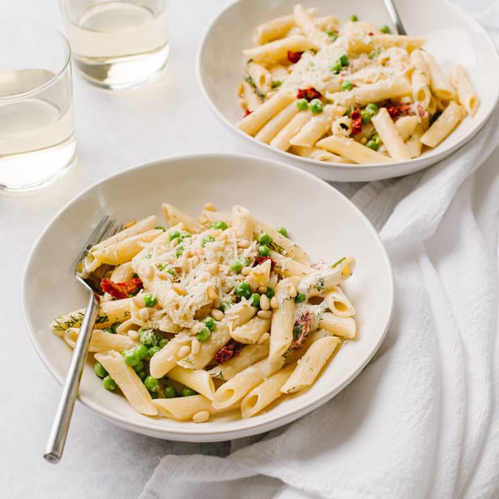 creamy pasta with boursin cheese and green peas in two white bowls with glasses of white wine