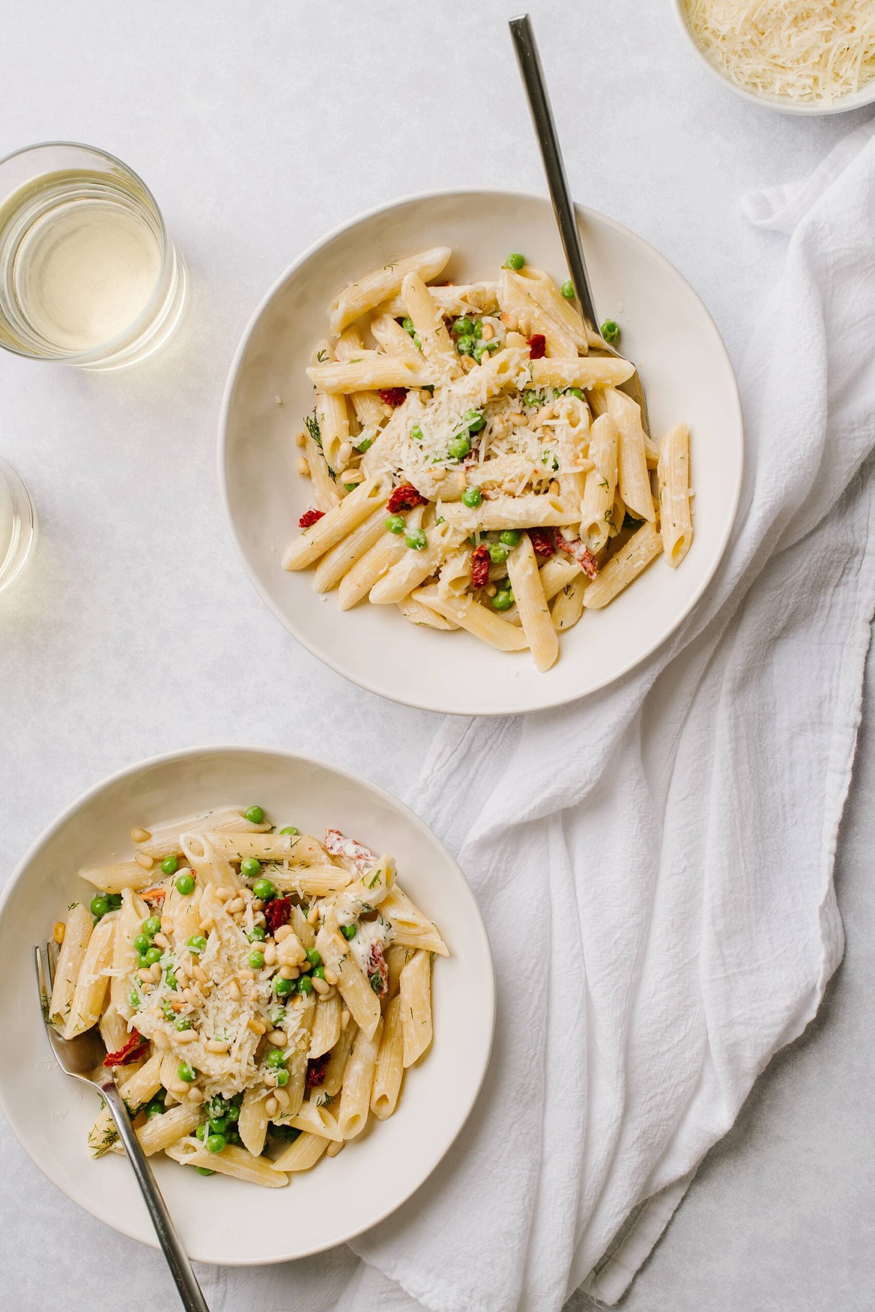 creamy pasta with boursin cheese and green peas in two white bowls with glasses of white wine