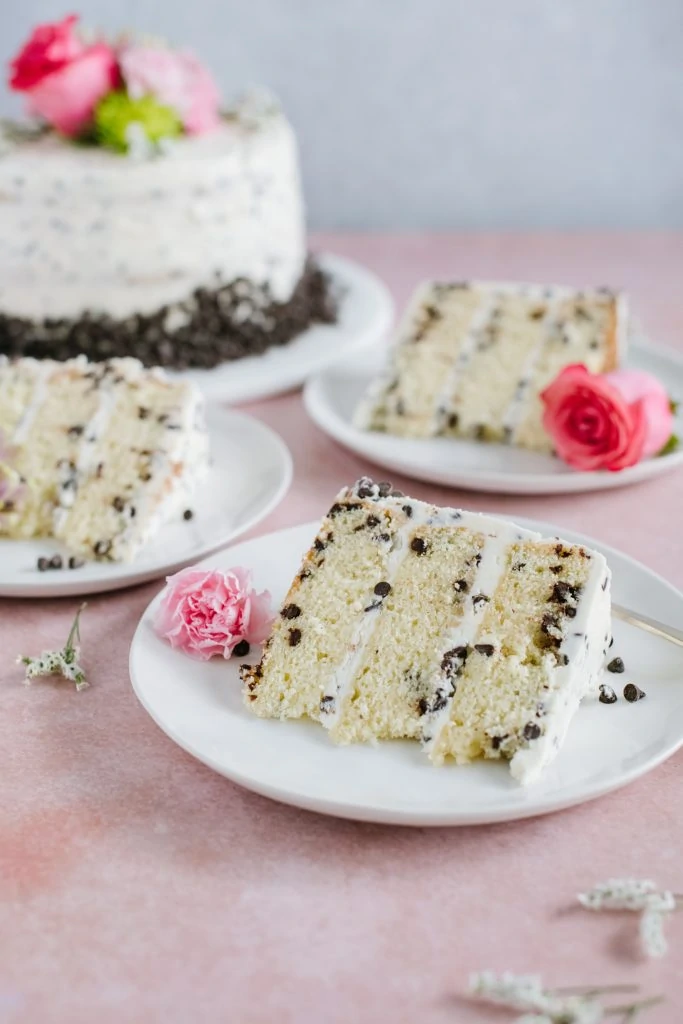 three slices of yellow cake with chocolate chips and buttercream on white plate with cake in background